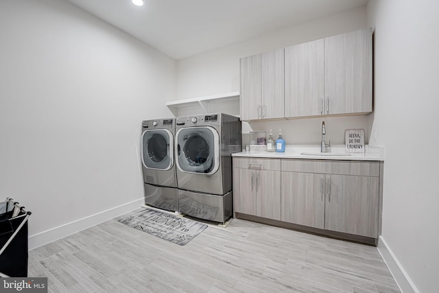 clothes washing area featuring a sink, washer and dryer, cabinet space, light wood-style floors, and baseboards