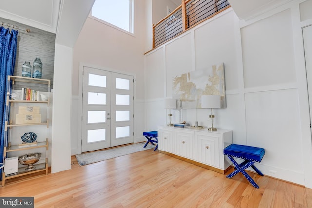 foyer with french doors, wood finished floors, a towering ceiling, and a decorative wall