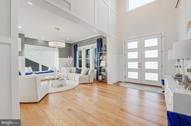 entryway with french doors, light wood-style floors, a chandelier, and a towering ceiling