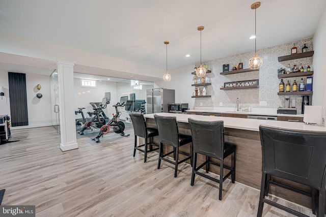 bar featuring a sink, indoor wet bar, light wood-style floors, appliances with stainless steel finishes, and tasteful backsplash