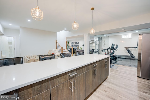 kitchen with light countertops, light wood-type flooring, freestanding refrigerator, and pendant lighting