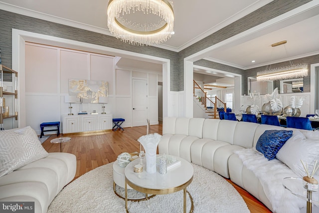 living area featuring stairs, wood finished floors, crown molding, and a decorative wall