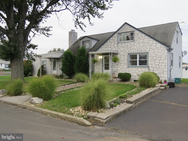 view of front of house featuring a shingled roof, stone siding, a chimney, and a front lawn