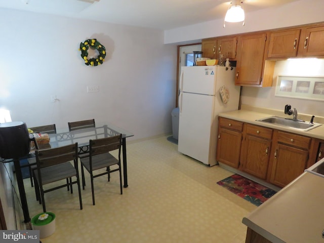 kitchen with a sink, light countertops, freestanding refrigerator, light floors, and brown cabinetry