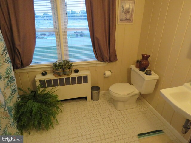 bathroom featuring toilet, radiator heating unit, wooden walls, and baseboards