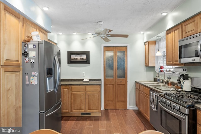 kitchen featuring appliances with stainless steel finishes, wood tiled floor, brown cabinetry, a sink, and ceiling fan