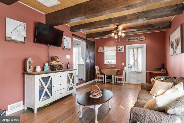 living room with a barn door, visible vents, wood finished floors, and beamed ceiling