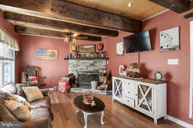 living area with a glass covered fireplace, beam ceiling, baseboards, and wood finished floors