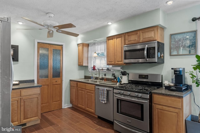 kitchen featuring dark countertops, ceiling fan, dark wood-type flooring, stainless steel appliances, and a sink