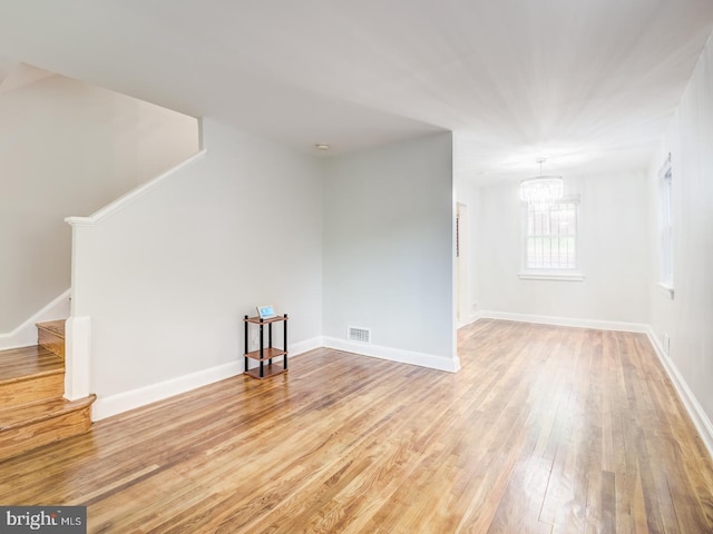 unfurnished living room featuring stairway, baseboards, visible vents, and hardwood / wood-style floors