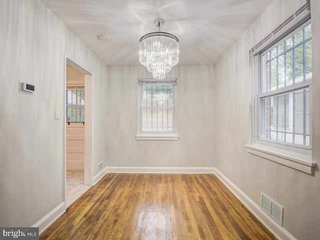 unfurnished dining area with visible vents, baseboards, an inviting chandelier, and hardwood / wood-style floors