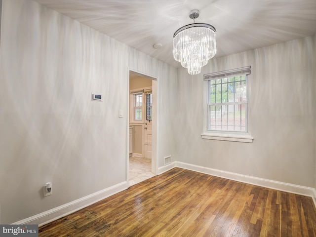 spare room featuring a notable chandelier, visible vents, baseboards, and hardwood / wood-style floors