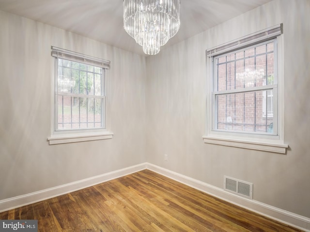 empty room featuring a chandelier, visible vents, baseboards, and wood finished floors