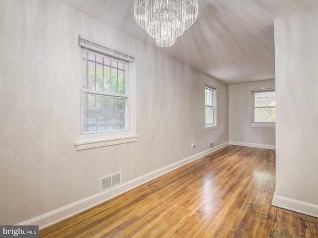 empty room featuring hardwood / wood-style flooring, baseboards, visible vents, and a chandelier