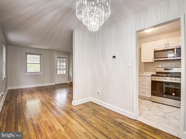 unfurnished dining area with light wood-type flooring, baseboards, and a notable chandelier