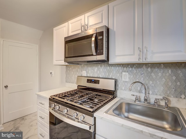 kitchen featuring backsplash, white cabinets, marble finish floor, stainless steel appliances, and a sink