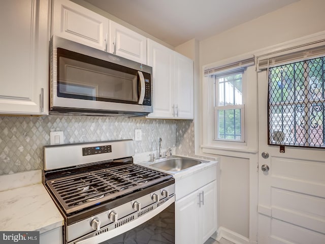 kitchen featuring light stone countertops, a sink, appliances with stainless steel finishes, white cabinetry, and backsplash