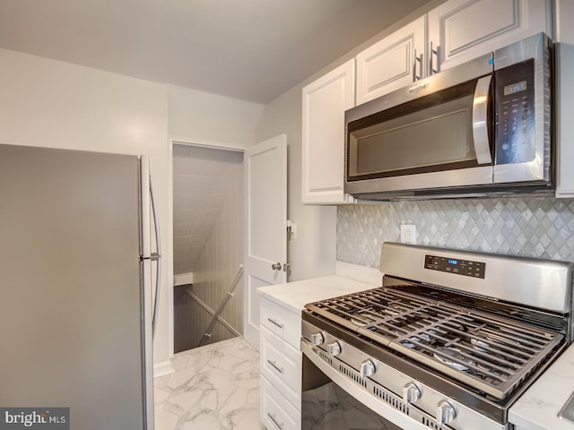 kitchen with light stone countertops, stainless steel appliances, white cabinets, marble finish floor, and tasteful backsplash