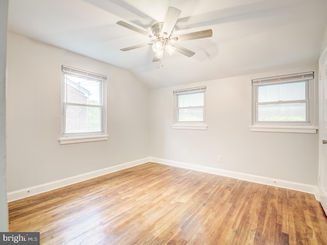 spare room with baseboards, plenty of natural light, light wood-style flooring, and vaulted ceiling