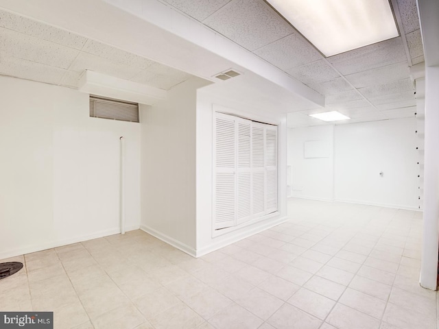 finished basement featuring a paneled ceiling, visible vents, and baseboards