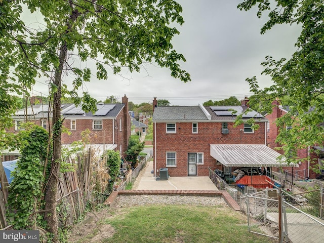 back of house featuring a lawn, roof mounted solar panels, a fenced backyard, brick siding, and a patio area