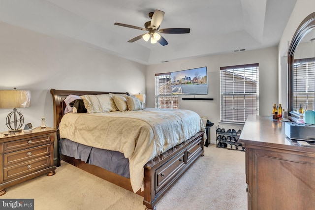 bedroom featuring visible vents, baseboards, light colored carpet, ceiling fan, and a tray ceiling