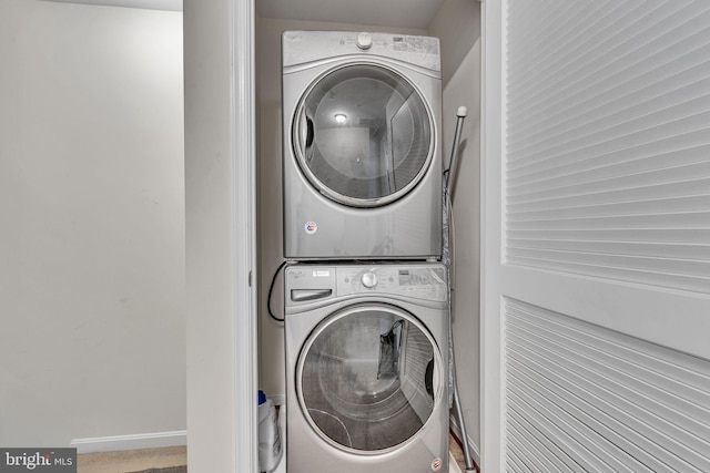 clothes washing area featuring laundry area, stacked washer / dryer, and baseboards