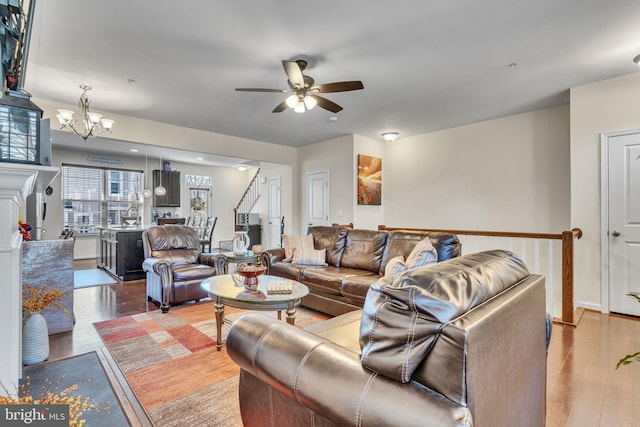 living room featuring ceiling fan with notable chandelier, stairway, and wood finished floors