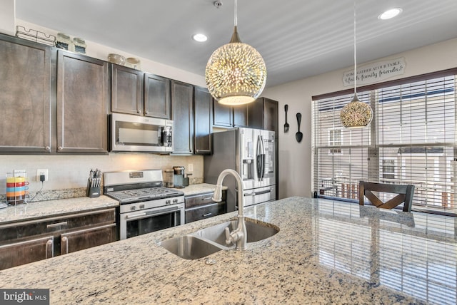 kitchen with decorative light fixtures, stainless steel appliances, backsplash, a sink, and dark brown cabinets