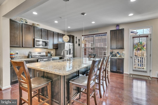 kitchen featuring appliances with stainless steel finishes, dark brown cabinets, a sink, and a kitchen breakfast bar