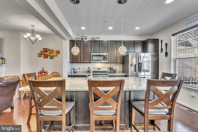 kitchen featuring visible vents, appliances with stainless steel finishes, decorative light fixtures, dark brown cabinets, and light wood-type flooring