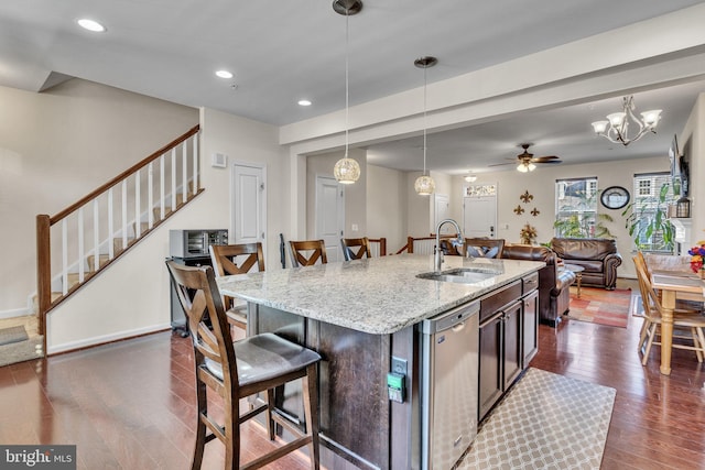 kitchen with dark wood-type flooring, a sink, light stone countertops, hanging light fixtures, and stainless steel dishwasher