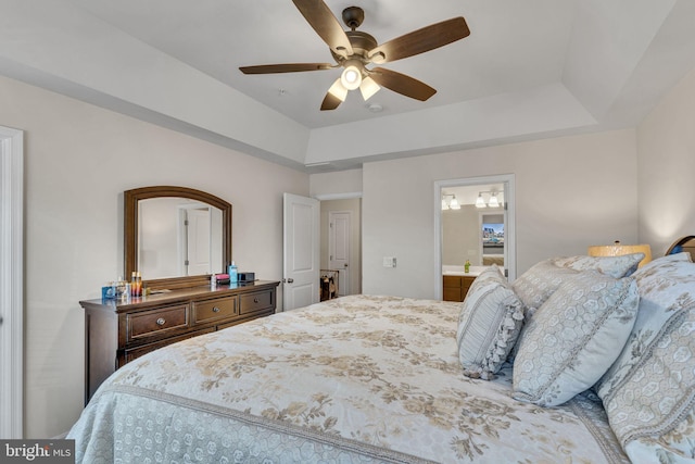 bedroom featuring ensuite bath, a tray ceiling, and a ceiling fan