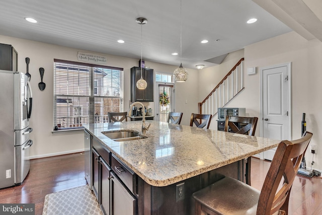 kitchen with dark wood-style floors, stainless steel appliances, a sink, an island with sink, and a kitchen breakfast bar