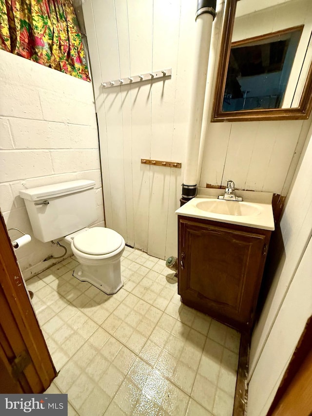 bathroom featuring toilet, tile patterned floors, concrete block wall, and vanity