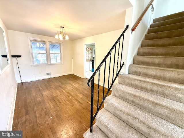 staircase featuring baseboards, wood finished floors, visible vents, and a notable chandelier