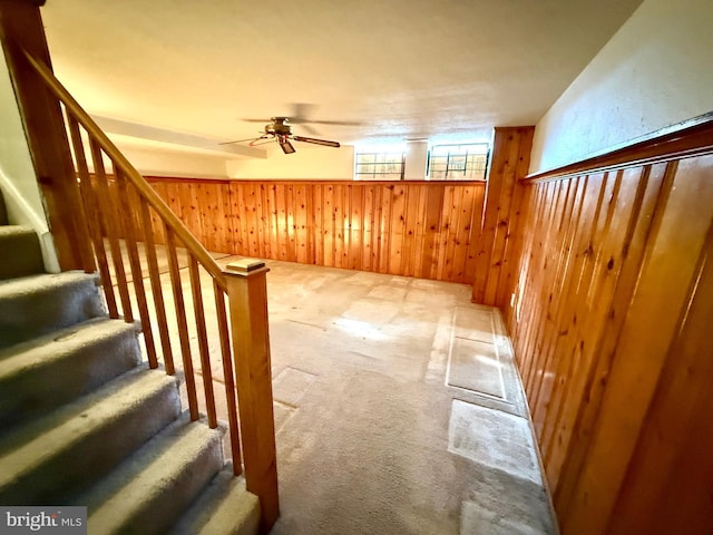 interior space featuring carpet, wood walls, stairway, and ceiling fan