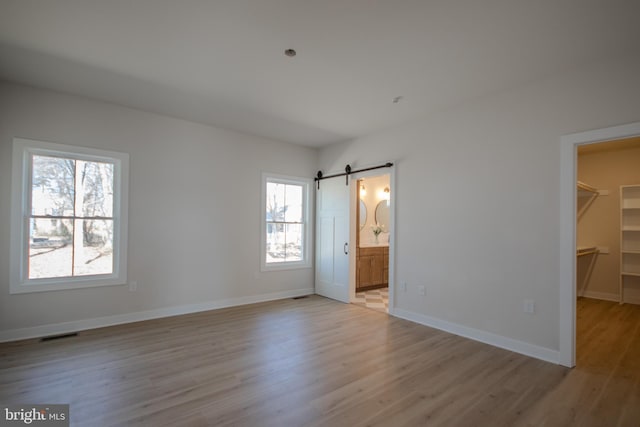 unfurnished bedroom featuring visible vents, light wood-style flooring, a walk in closet, and a barn door