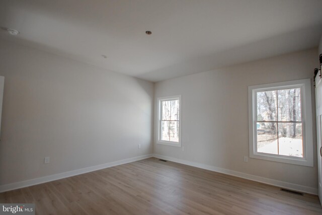 unfurnished room with light wood finished floors, visible vents, and baseboards