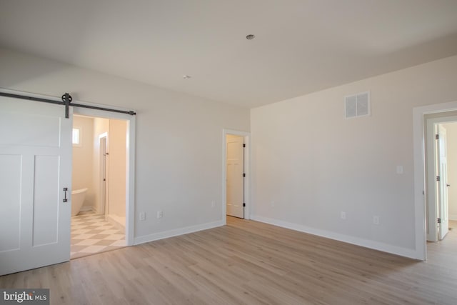 unfurnished bedroom featuring a barn door, light wood-style floors, visible vents, and baseboards