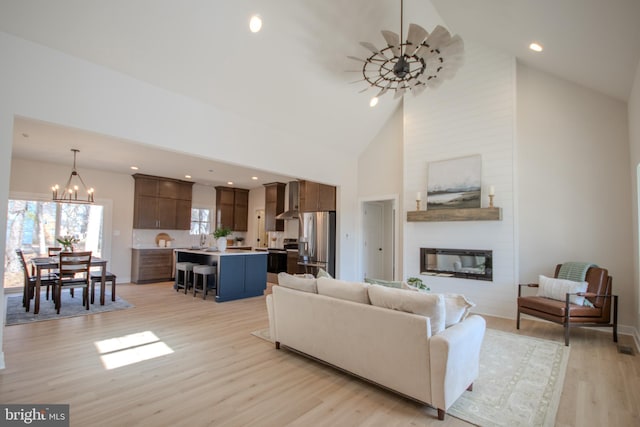 living room with high vaulted ceiling, an inviting chandelier, light wood-style flooring, recessed lighting, and a fireplace