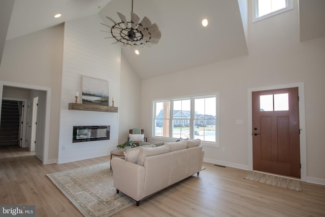 living area featuring high vaulted ceiling, a fireplace, light wood finished floors, baseboards, and ceiling fan