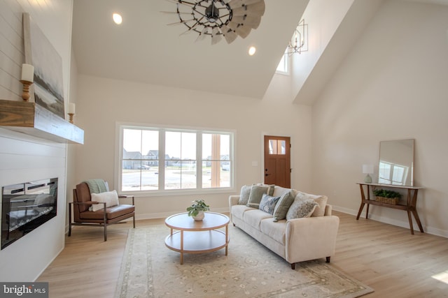 living room featuring baseboards, light wood finished floors, high vaulted ceiling, recessed lighting, and a glass covered fireplace