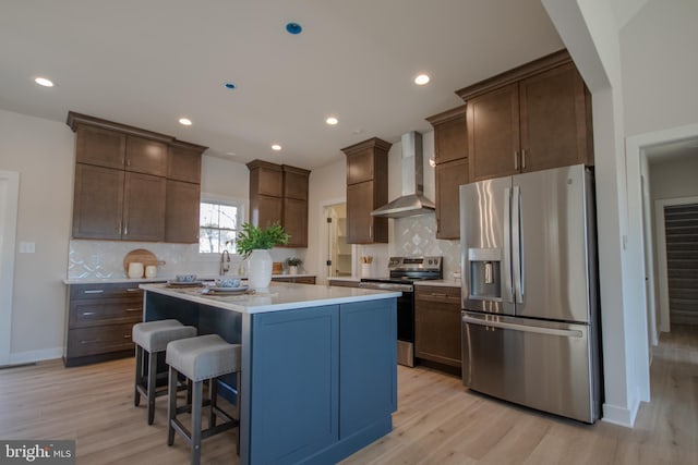 kitchen with appliances with stainless steel finishes, a center island, light wood-style floors, and wall chimney range hood