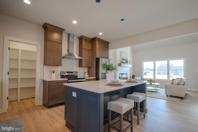 kitchen featuring a kitchen island, a breakfast bar, light wood-style flooring, appliances with stainless steel finishes, and wall chimney range hood