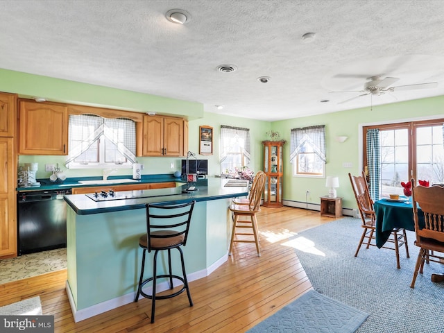 kitchen featuring light wood-type flooring, black appliances, a breakfast bar, and visible vents