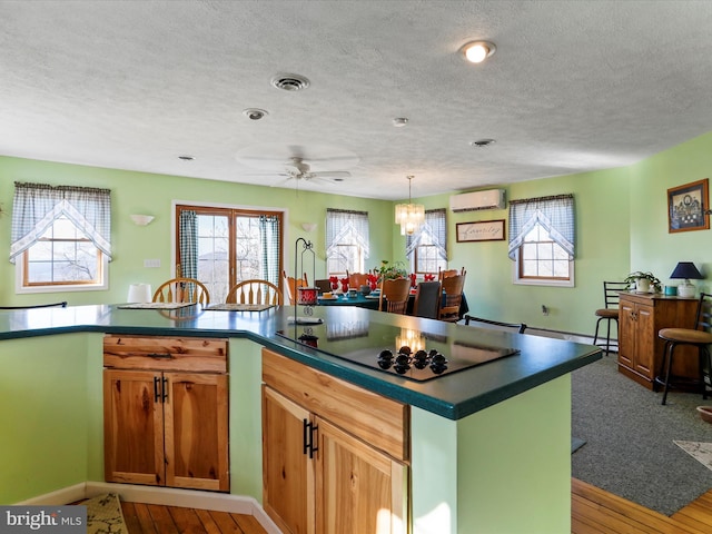 kitchen featuring a wall mounted AC, black electric stovetop, dark countertops, visible vents, and ceiling fan
