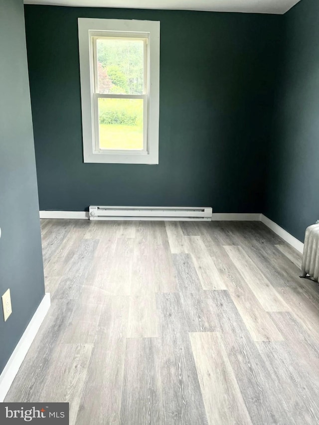 empty room featuring wood finished floors, baseboards, and baseboard heating