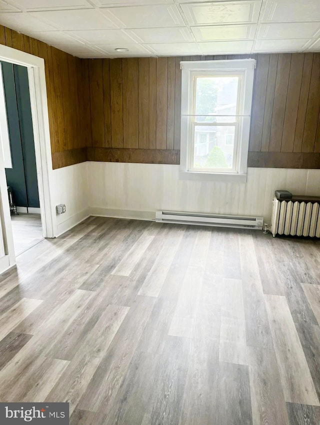 empty room with light wood-type flooring, wood walls, and a baseboard radiator