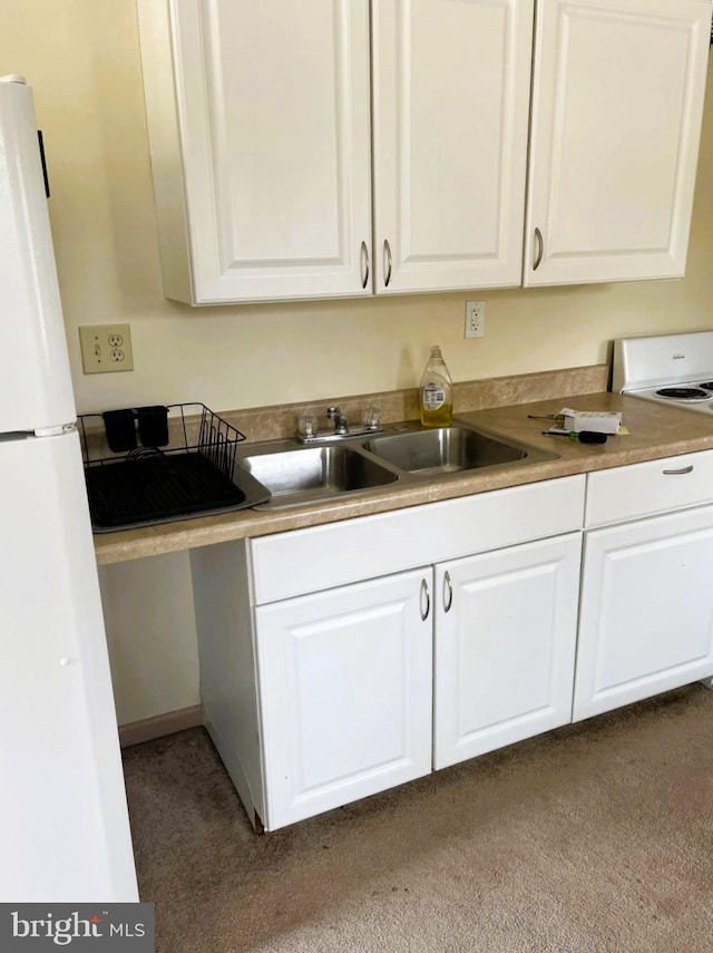 kitchen featuring stove, white cabinets, freestanding refrigerator, and a sink